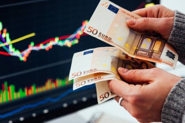 Borsa ekranının önünde Avrupa para birimi Euro 'yu tutan eller ticaret grafiklerini gösteriyor.