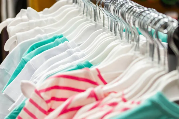 Cotton t-shirts on a hanger in a clothing store, background backdrop. Summer clothes supermarket T-shirt jacket white pink green