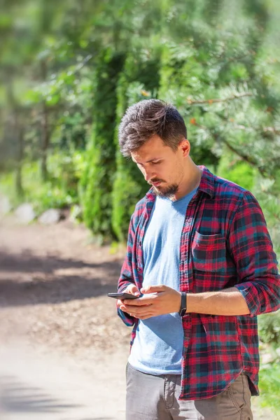 Young handsome Caucasian man with a beard and mustache writes on the phone. Modern man with a gadget, chatting, sending messages — Stock Photo, Image