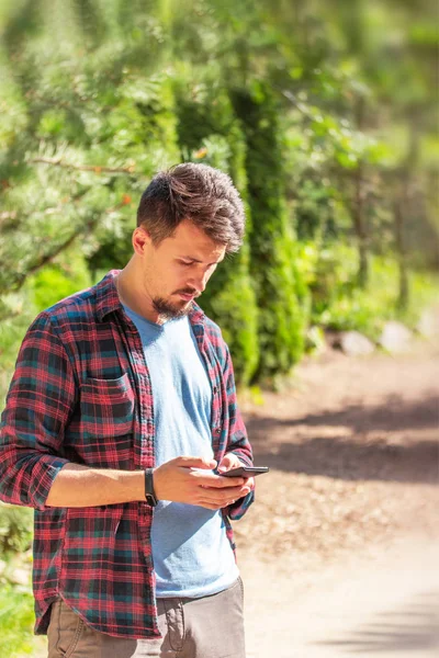 Young handsome Caucasian man writes on the phone, chatting, sending messages. Man in the park waiting for a date — Stock Photo, Image