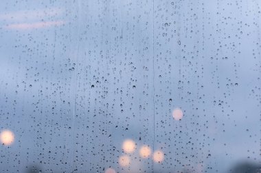 Pencerenin cam yüzeyinde büyük yağmur damlaları sağanak yağış, akşam ışıkları sönüyor. Arkaplan duvar kağıdı arkaplanı