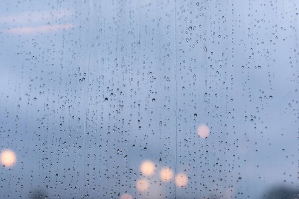 Крупные капли дождя на стеклянную поверхность окна, ливни дождя, вечерние огни города разряжаются. Фон обои фона
