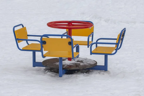 Leere Spielplatz im Winter, kaltes Wetter, niedrige Temperaturen, Schaukel gelb rot blau Metall bunte lustige Minikarussell. weißer Schnee ohne Menschen — Stockfoto