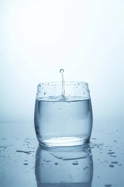 A splash of water in a glass, a drop of water hanging in the air, pure drinking spring clear water, a splash with a drop of water — Stock Photo, Image