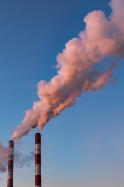 Gün batımında kalın pembe dumanlı bir kazan dairesinin iki borusu. Güzel pembe buhar, açık mavi gökyüzü. Hava kirliliği, çevre sorunları, hava emisyonları