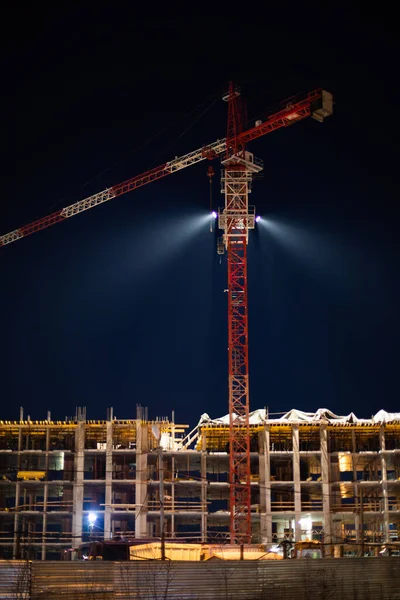 Night shooting, construction of an apartment building, erection of the floors of a multi-storey building. Construction crane lighting a construction site at night