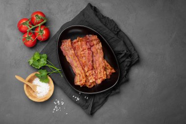 Gri arka planda siyah tabakta kızarmış domuz pastırması..