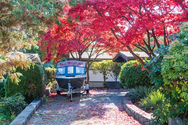 Boat in front of the autumn trees on a backyard. Small motor boat on a trailer staying on a backyard under a colored autumn trees in sunny weather.