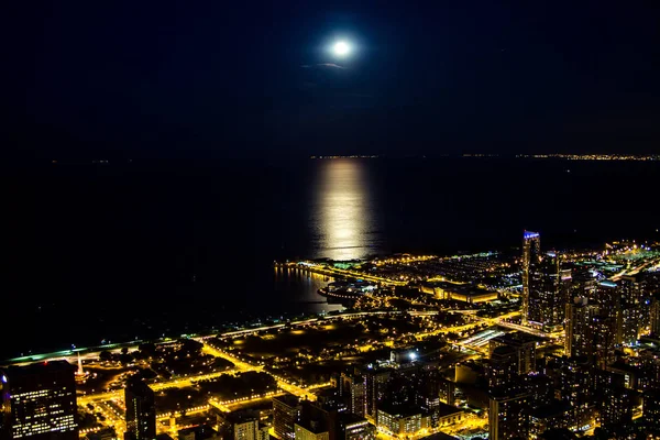 Night city lights with moonlight on the lake. Dark night skyline, city lights fill all the streets and highways, moonlight runs from the far horizon to the very city on the flat and soft lake surface.