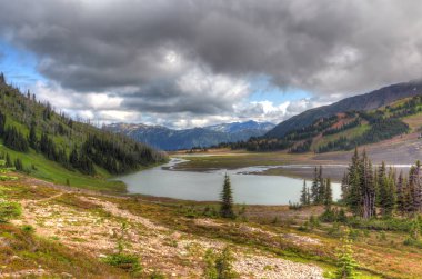 Kuzey Amerika 'nın yüksek karlı dağları manzaralı bulutlar ve altında bir buzul gölü.