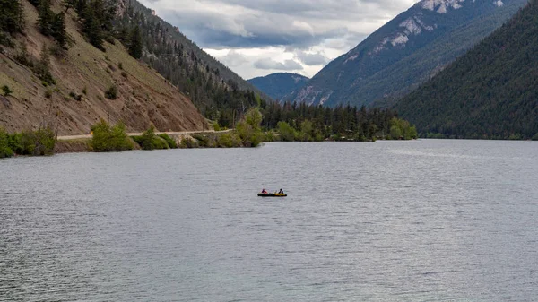 Large lake surface surrounded by tall mountains, a sole person in a kayak rowing on the water
