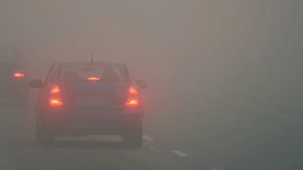 Auto 's in de mist. Slecht winterweer en gevaarlijk autoverkeer op de weg. Lichte voertuigen in mist. — Stockfoto