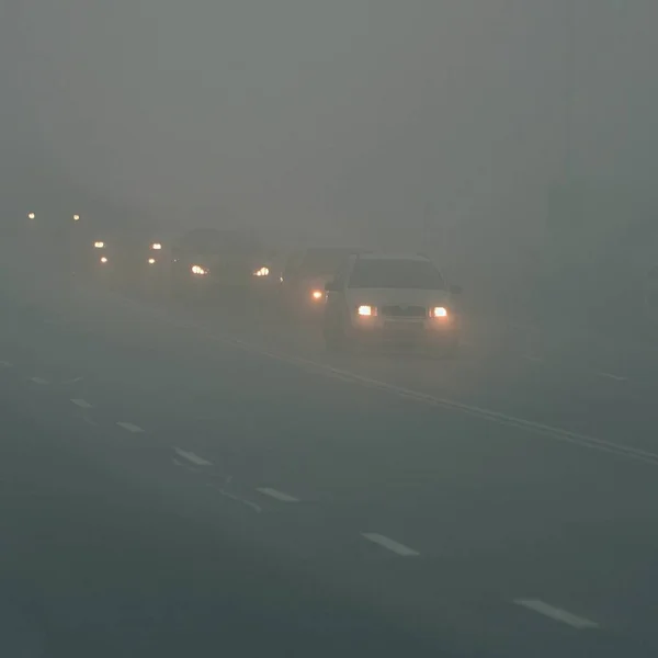 Carros no nevoeiro. Mau tempo de inverno e tráfego automóvel perigoso na estrada. Veículos ligeiros no nevoeiro. — Fotografia de Stock