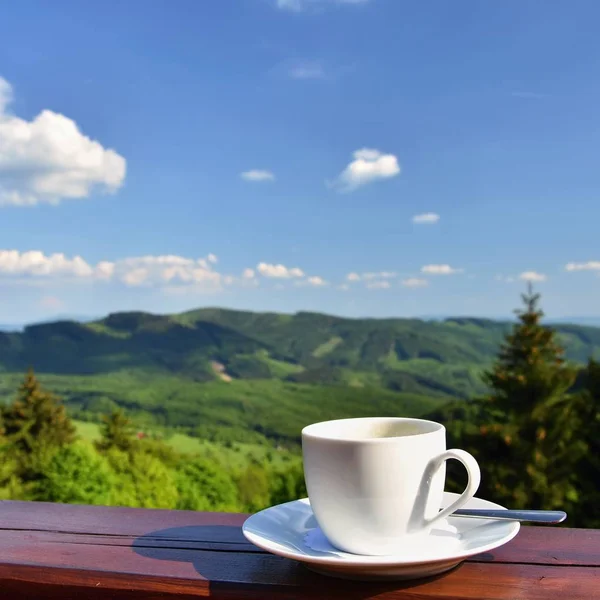 Weiße Tasse heißen Kaffee auf Balkon mit Natur und Bergen