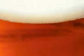 Pivo. Krásný detail vyšlapané sklenici piva s pěnou. Abstraktní barevné pozadí.