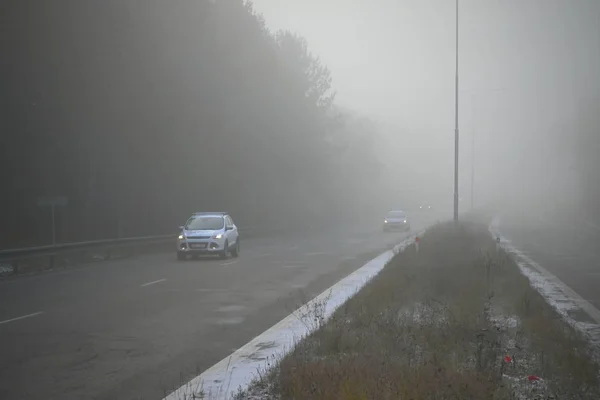 Autos im Nebel. Schlechtes Winterwetter und gefährlicher Autoverkehr auf den Straßen. Leichtfahrzeuge bei nebligem Tag. — Stockfoto