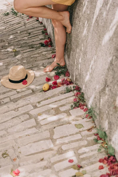 夏のドレスを着た女の子の足には、石畳の階段の村の地中海のわら帽子が付いています — ストック写真
