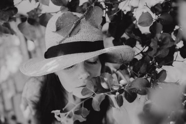 Akdeniz 'de yazın çiçek açan ağaçların altında hasır şapkalı bir kızın siyah beyaz portresi. 