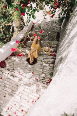 Sarı elbiseli, uzun kahverengi saçlı bir kız, merdivenlerde uzanıyor, pembe begonvil çiçeklerinin arka planında, yazın Akdeniz 'de, tatilde.
