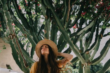 Sarı elbiseli ve uzun kahverengi saçlı bir kız yeşil çiçekli kaktüs ve pembe bougainvillea çiçeklerinin arka planında, Akdeniz 'de tatilde.