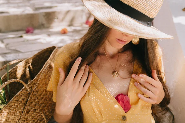 Fille dans une robe jaune et chapeau avec de longs cheveux bruns, est assis sur les marches, sur le fond de cactus à fleurs vertes et fleurs de bougainvilliers roses, en été en Méditerranée, en vacances — Photo