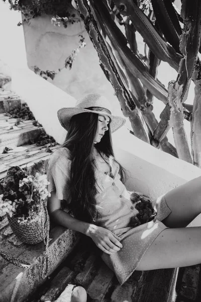 Portrait noir et blanc de fille en chapeau aux cheveux longs, assise sur les marches, à côté des fleurs de cactus et de bougainvilliers en fleurs, en été en Méditerranée, en vacances — Photo