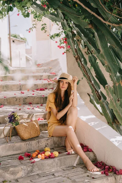 Sarı elbiseli ve uzun kahverengi saçlı bir kız yeşil çiçekli kaktüs ve pembe bougainvillea çiçeklerinin arka planında, Akdeniz 'de tatilde.