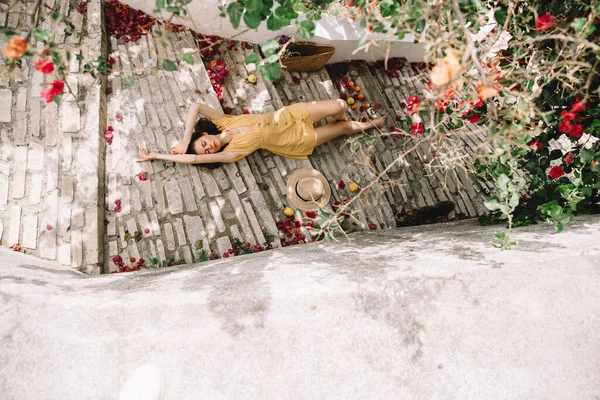 長い茶色の髪をした黄色のドレスの女の子は階段の上にありピンクのブーゲンビリアの花の背景の上のビュー地中海の夏休暇に — ストック写真