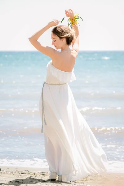 Panna młoda na morzu. Ceremonia ślubna na morzu, na plaży. Tło morza i drzewa mimozy. Młoda panna młoda jest ubrana w białą sukienkę w stylu greckim. — Zdjęcie stockowe