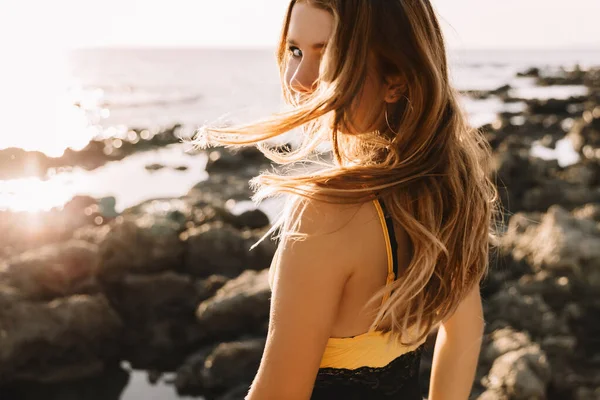 Dívka v plavkách si užívá a prochází se po pláži, v létě, při západu slunce. Portrét šťastné mladé ženy usmívající se na moře. — Stock fotografie