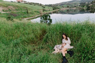 Anne ve kız bebek çimenlerde uzanıyor, mutlu, uyumlu bir aile açık havada, baharda doğada, dağlarda gülüyor ve oynuyor.