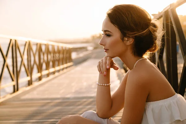 Retrato de una hermosa joven sonriente en el vestido blanco en estilo griego caminando a lo largo del paseo marítimo. Verano, hora del atardecer. Boda de novia en el mar —  Fotos de Stock