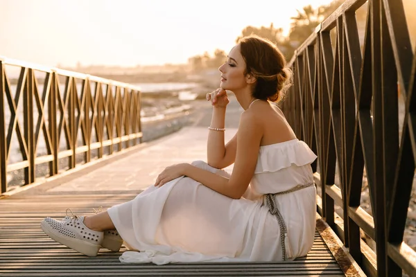 Retrato de una hermosa joven sonriente en el vestido blanco en estilo griego caminando a lo largo del paseo marítimo. Verano, hora del atardecer. Boda de novia en el mar —  Fotos de Stock