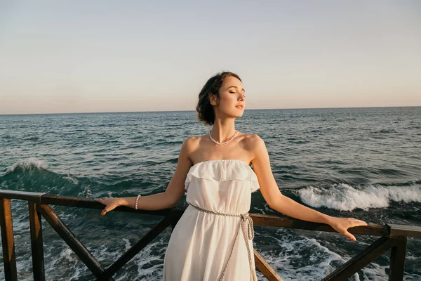 Belle jeune fille souriante dans la robe blanche de style grec marchant le long de la promenade maritime. L'été, au coucher du soleil. Mariage de mariée en mer — Photo
