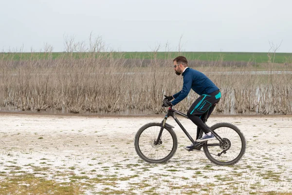 Cyclist on a mountain bike on a salt beach on a background of reeds and a lake