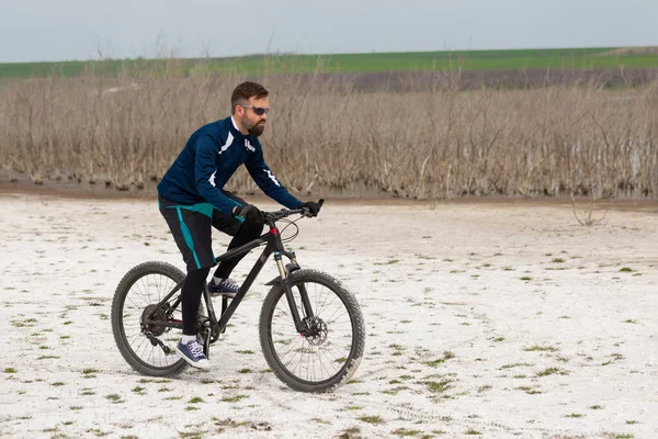 Cyclist on a mountain bike on a salt beach on a background of reeds and a lake