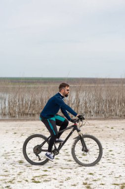 Bisikletçi, bir dağ bisikleti üzerinde, bir tuz plajında, arka planda sazlıklar ve bir gölde.