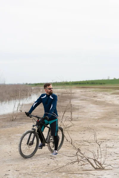 Cyclist on a mountain bike on a salt beach on a background of reeds and a lake