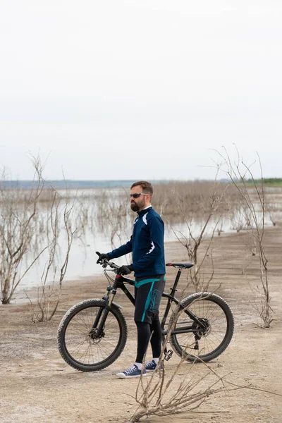 Cyclist on a mountain bike on a salt beach on a background of reeds and a lake