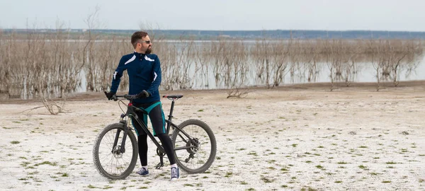 panorama cyclist on a mountain bike on a salt beach on a background of reeds and a lake