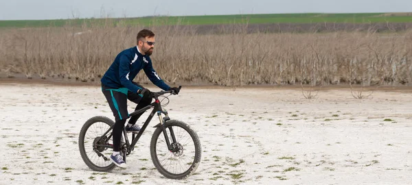 panorama cyclist on a mountain bike on a salt beach on a background of reeds and a lake