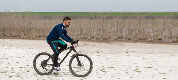 panorama cyclist on a mountain bike on a salt beach on a background of reeds and a lake