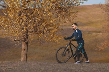 Bisikletçi sonbahar ormanlarında gezer ve park eder.