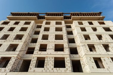 Mavi gökyüzünün arka planında yapım aşamasındaki çok katlı bir bina ve vinç.