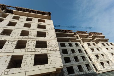 Mavi gökyüzünün arka planında yapım aşamasındaki çok katlı bir bina ve vinç.