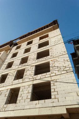 Mavi gökyüzünün arka planında yapım aşamasındaki çok katlı bir bina ve vinç.