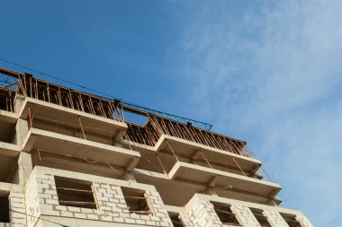 Mavi gökyüzünün arka planında yapım aşamasındaki çok katlı bir bina ve vinç.