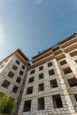 Mavi gökyüzünün arka planında yapım aşamasındaki çok katlı bir bina ve vinç.