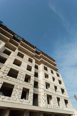 Mavi gökyüzünün arka planında yapım aşamasındaki çok katlı bir bina ve vinç.