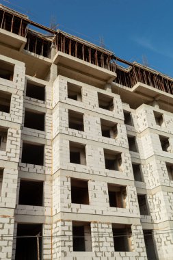 Mavi gökyüzünün arka planında yapım aşamasındaki çok katlı bir bina ve vinç.